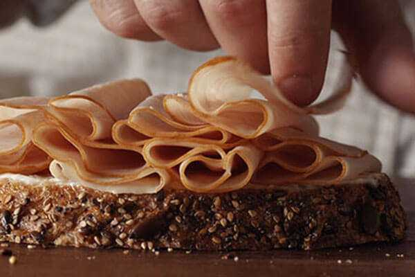 Sliced lunch meat being put on a slice of bread