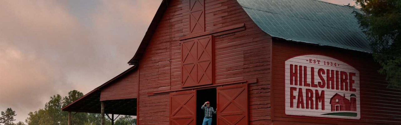 Red Barn with the Hillshire Farm logo on the side with a man standing in front of the barn